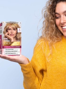 Modelo branca com cabelo loiro e cacheado segurando duas tintas da L'Oréal