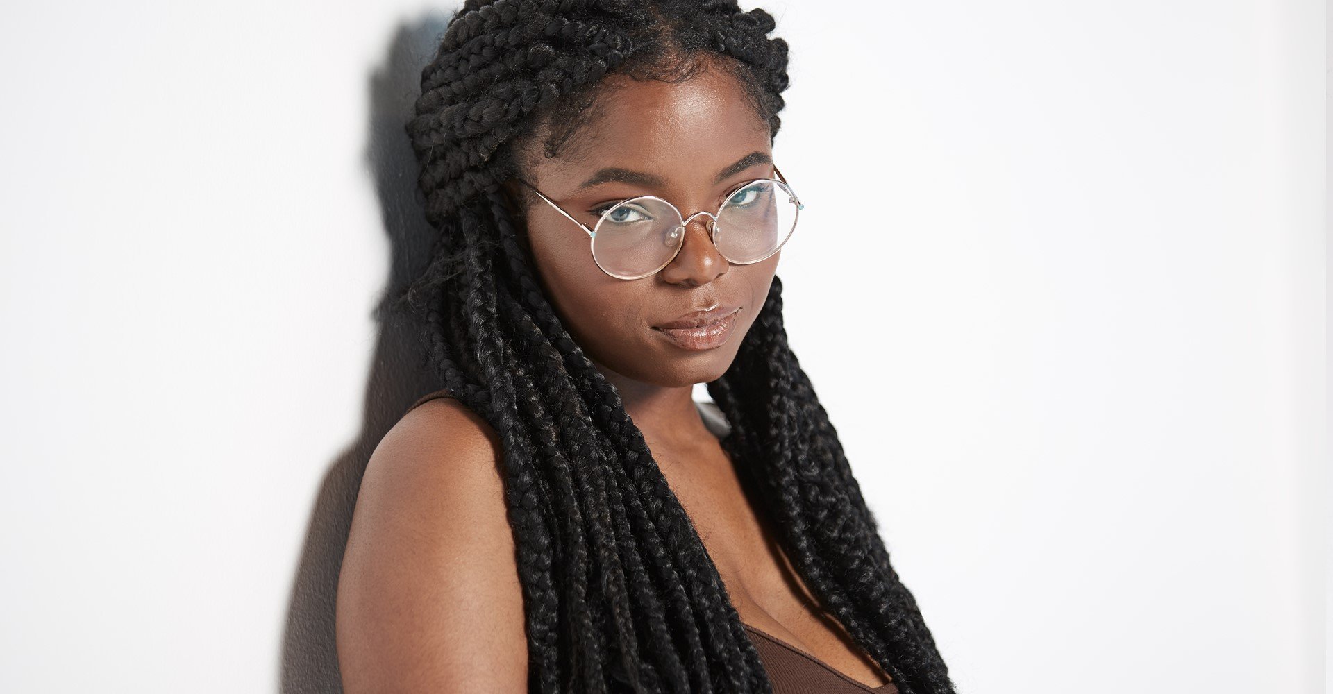 Modelo negra com tranças no cabelo e óculos de grau posando para a foto