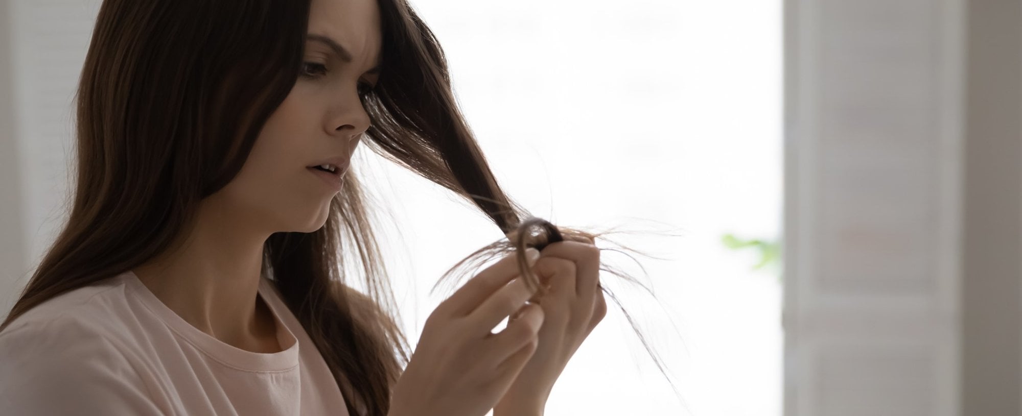 Modelo branca analisando as pontas do seu cabelo