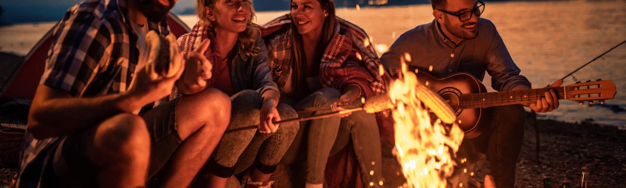 Grupos de amigos na praia conversando ao redor de uma fogueira