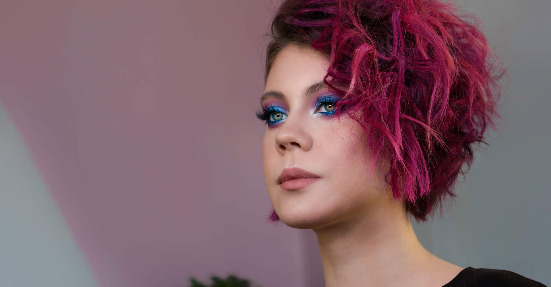 Modelo branca com sombra no olho azul e cabelo rosa escuro
