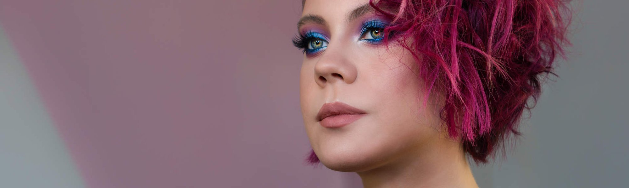 Modelo branca com sombra no olho azul e cabelo rosa escuro