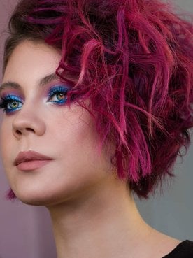 Modelo branca com sombra no olho azul e cabelo rosa escuro