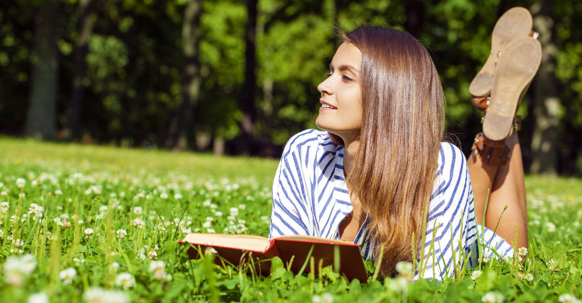 Modelo branca com cabelo liso deitada na grama lendo um livro