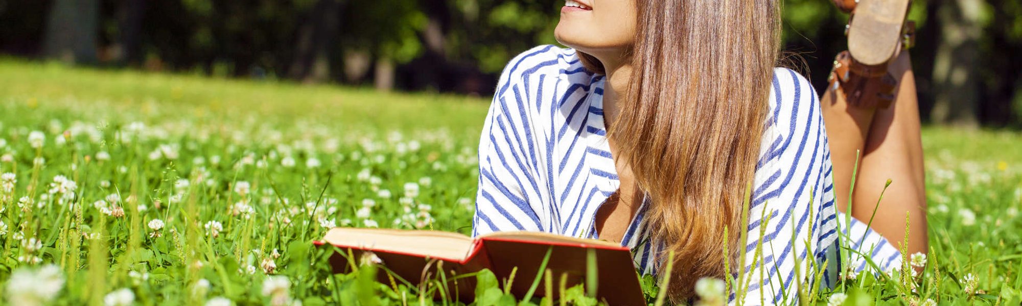 Modelo branca com cabelo liso deitada na grama lendo um livro