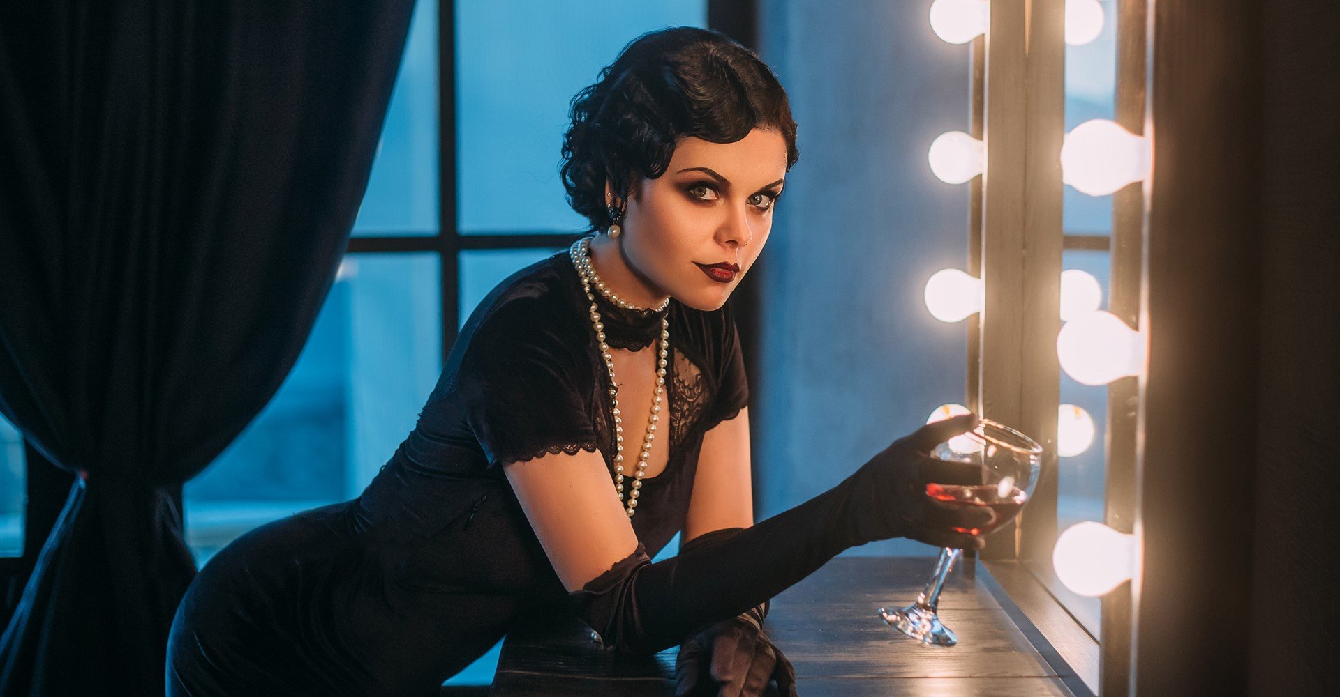 Modelo branca com vestido justo e preto, cabelo curto e com taça na mão