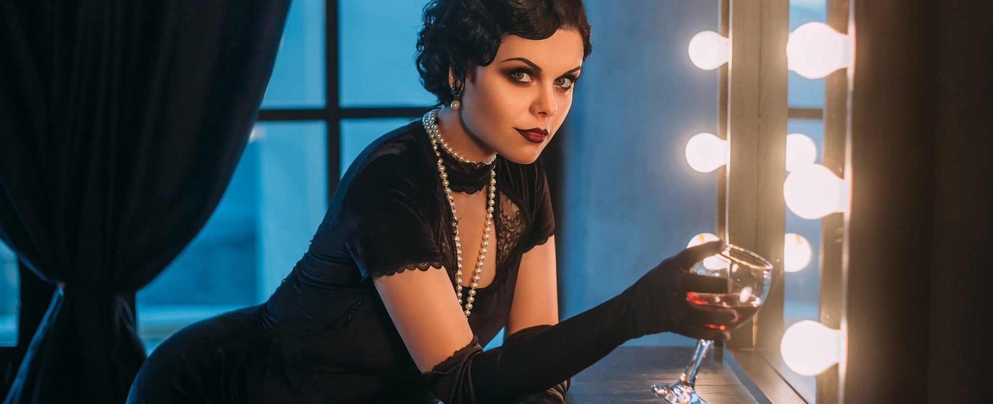 Modelo branca com vestido justo e preto, cabelo curto e com taça na mão