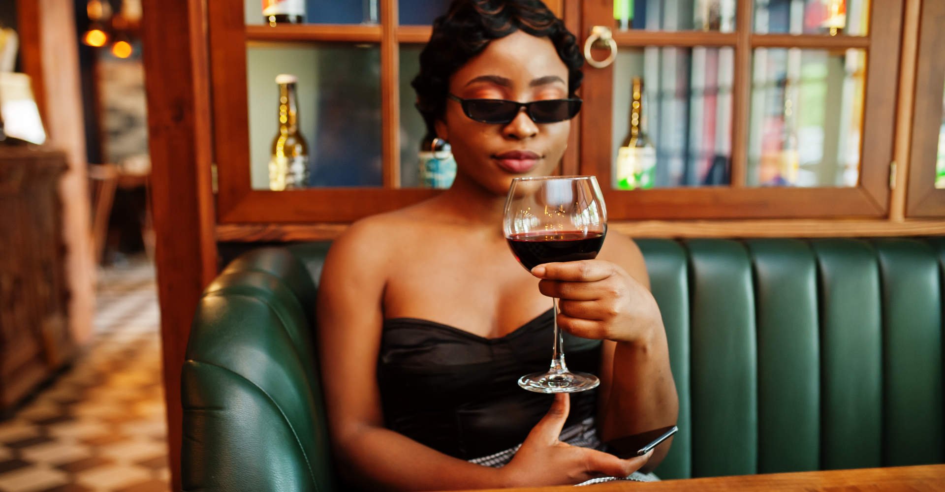 Modelo negra com cabelo curto, óculos de sol e taça na mão