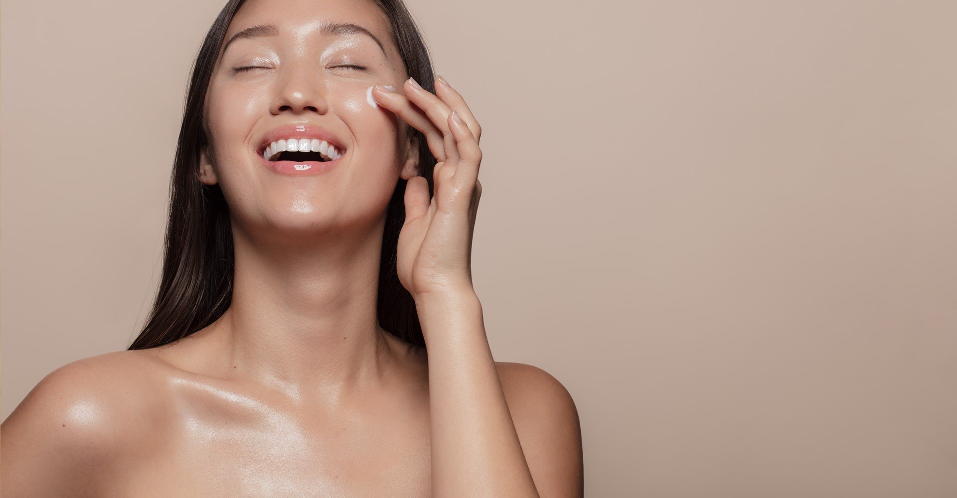 Modelo asiática sorrindo passando creme no rosto