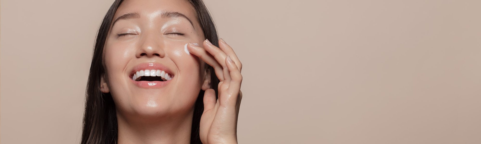 Modelo asiática sorrindo passando creme no rosto