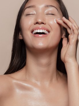 Modelo asiática sorrindo passando creme no rosto
