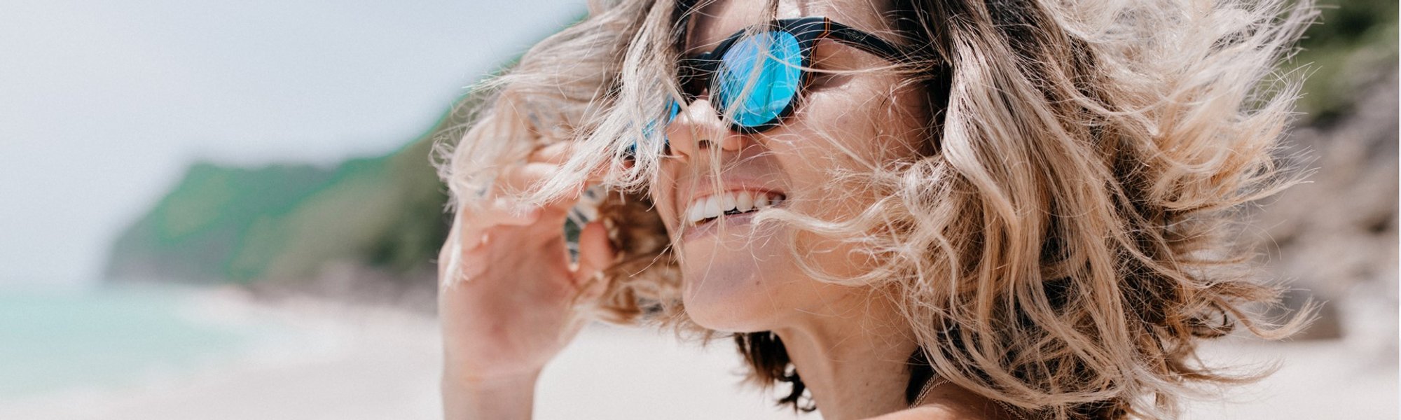 Modelo branca com óculos de sol e cabelo curto loiro na praia