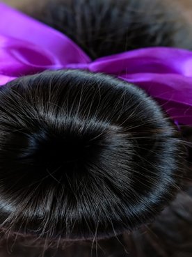Coque em cabelo preto com uma fita roxa