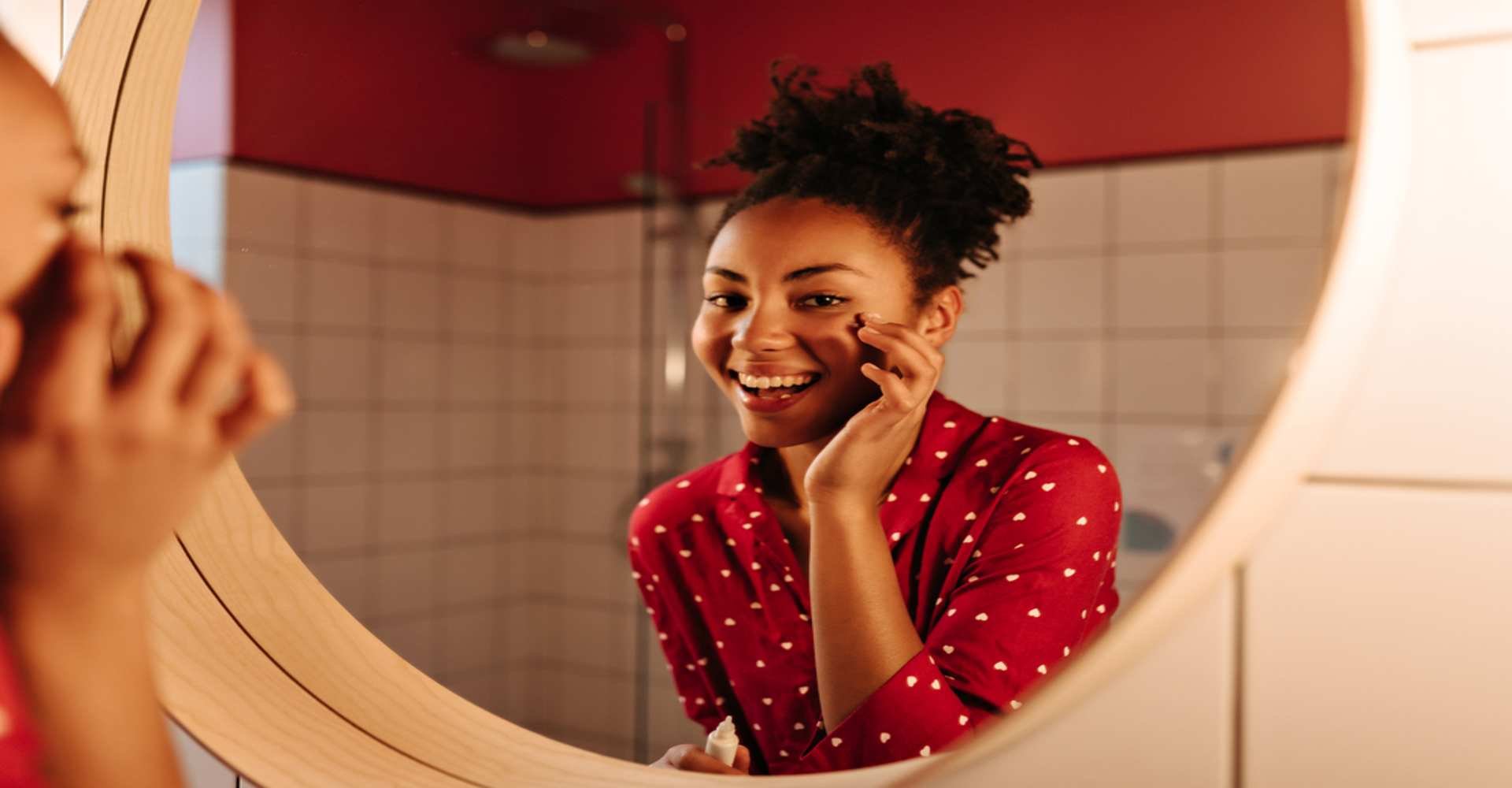 Modelo negra sorrindo se olhando no espelho com as mãos no rosto