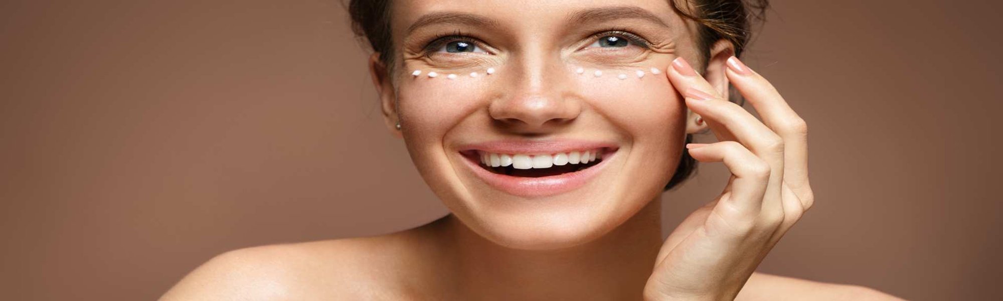 Modelo branca passando creme na área dos olhos