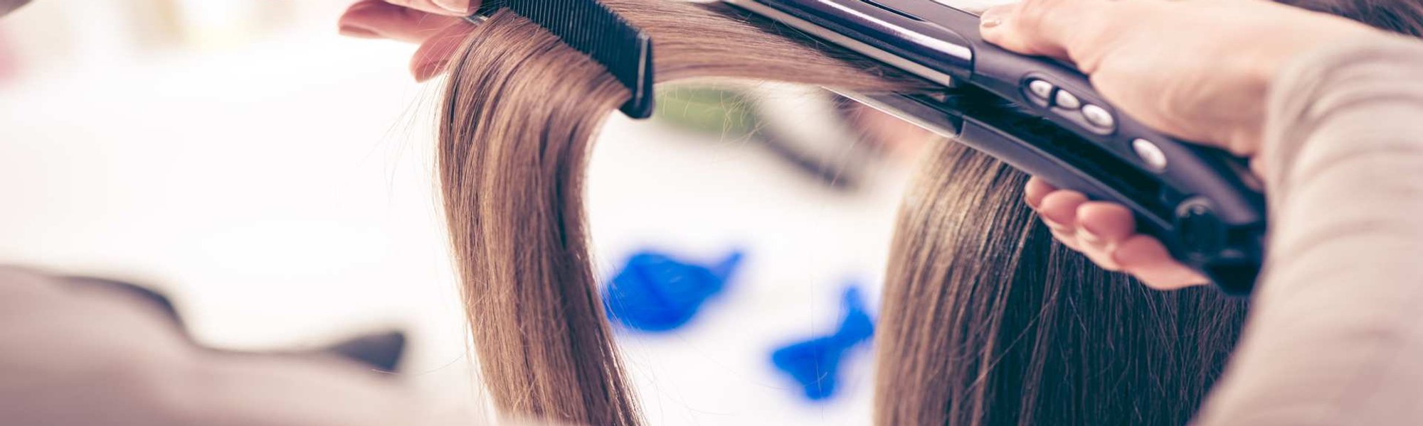 Modelo branca se olhando no espelho e passando chapinha no cabelo