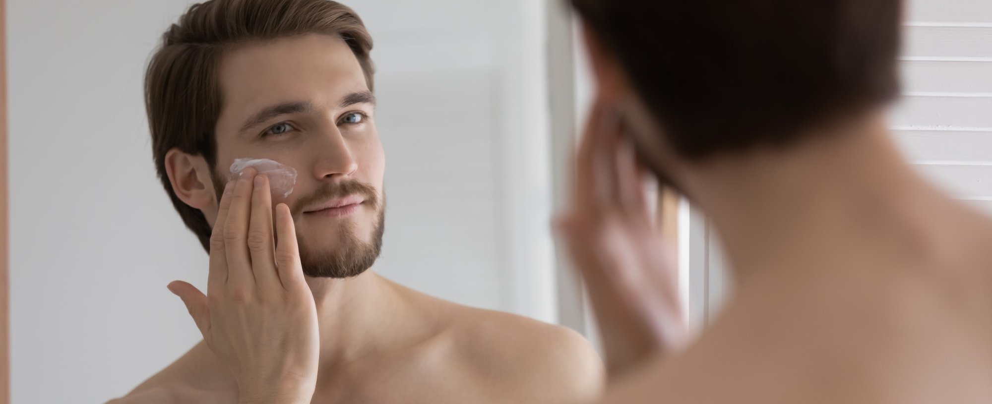 Homem se olhando no espelho passando creme no rosto