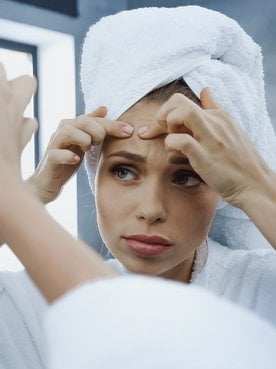 Modelo se olhando no espelho analisando acne