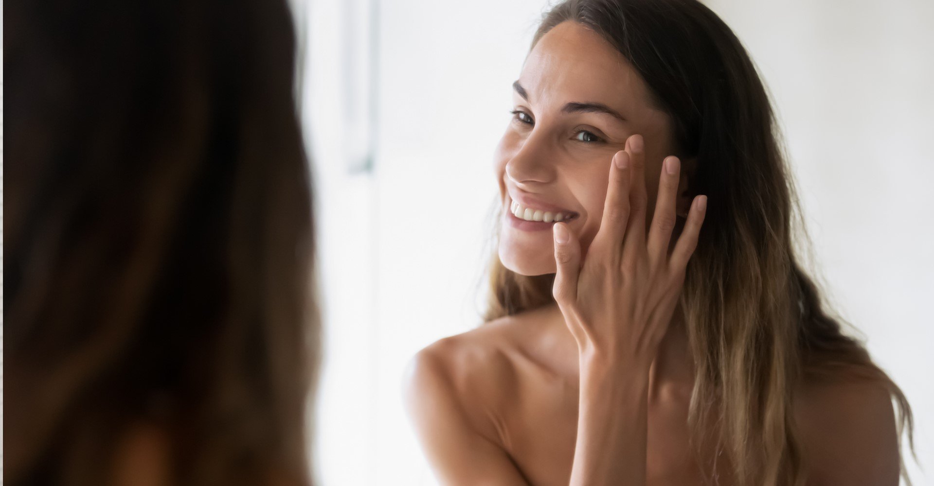 Modelo sorrindo se olhando no espelho e passando creme no cabelo