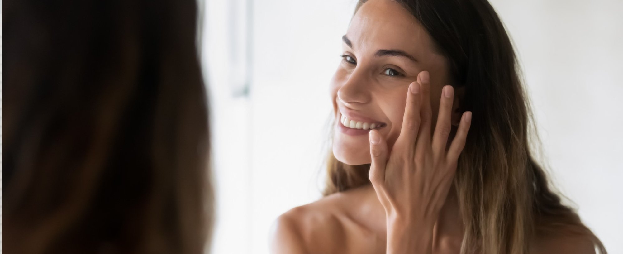 Modelo sorrindo se olhando no espelho e passando creme no cabelo