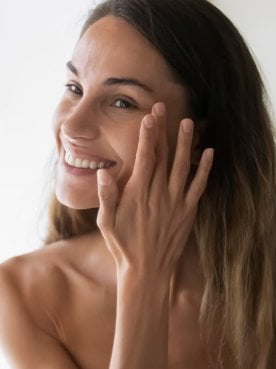 Modelo sorrindo se olhando no espelho e passando creme no cabelo