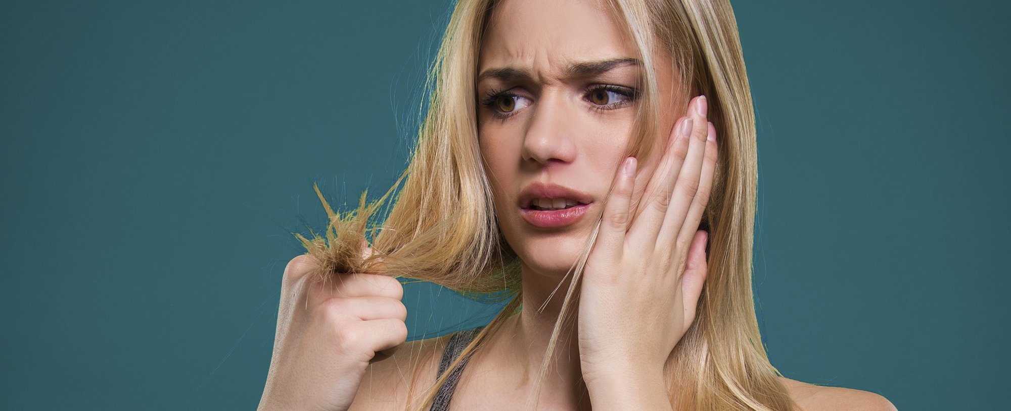Modelo branca e loirando analisando as pontas de seu cabelo