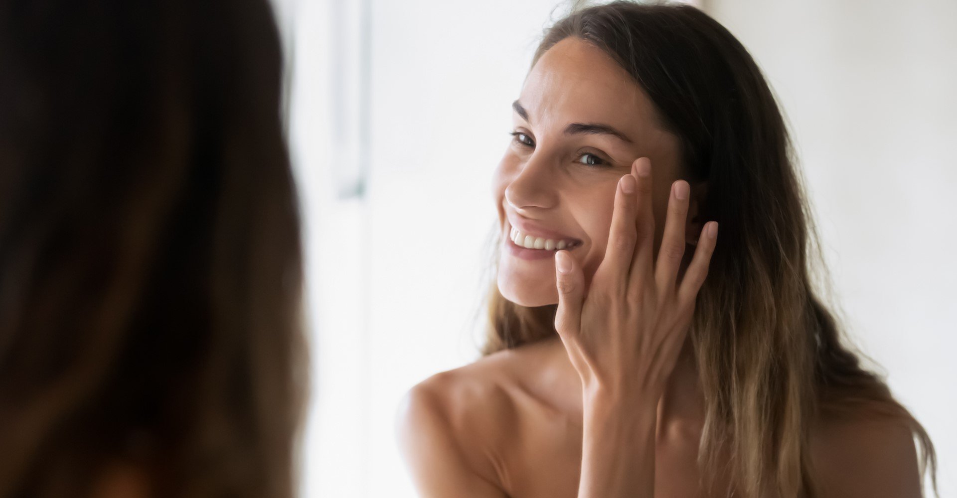 Modelo se olhando no espelho e passando creme no rosto