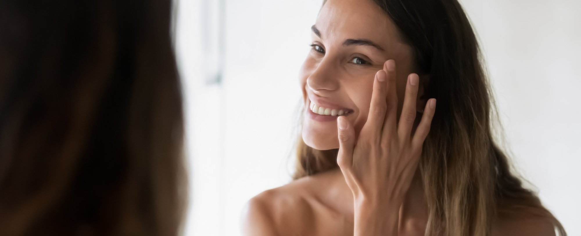 Modelo se olhando no espelho e passando creme no rosto