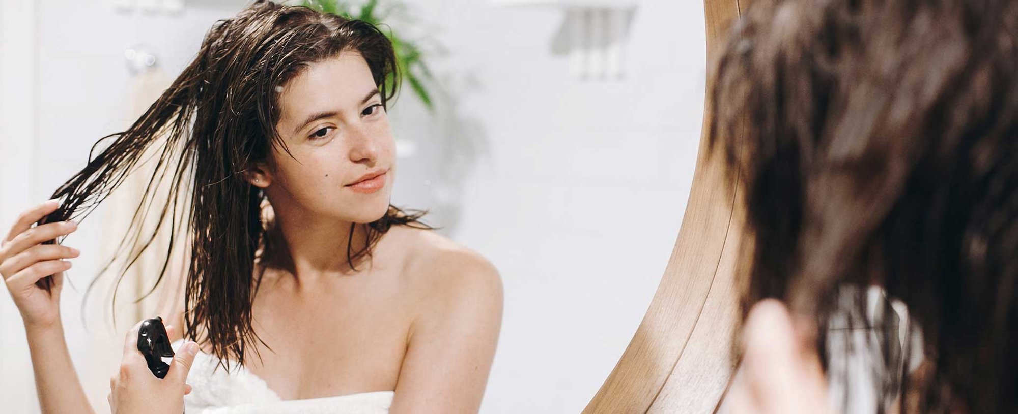 Mulher branca se olhando no espelho enquanto passa produto
