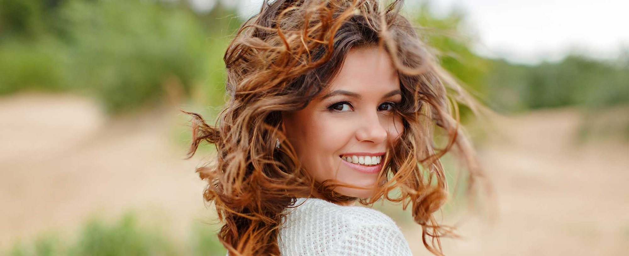Modelo branca com cabelo castanho ondulado sorrindo