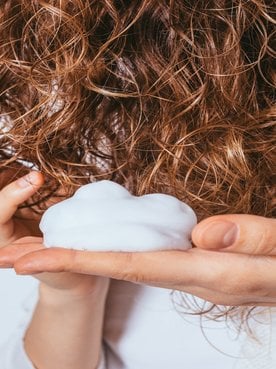 Imagens das mãos da modelo com mousse passando em seus cabelos loiros