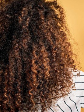 Mulher de costas cacheada com algumas madeixas mais claras