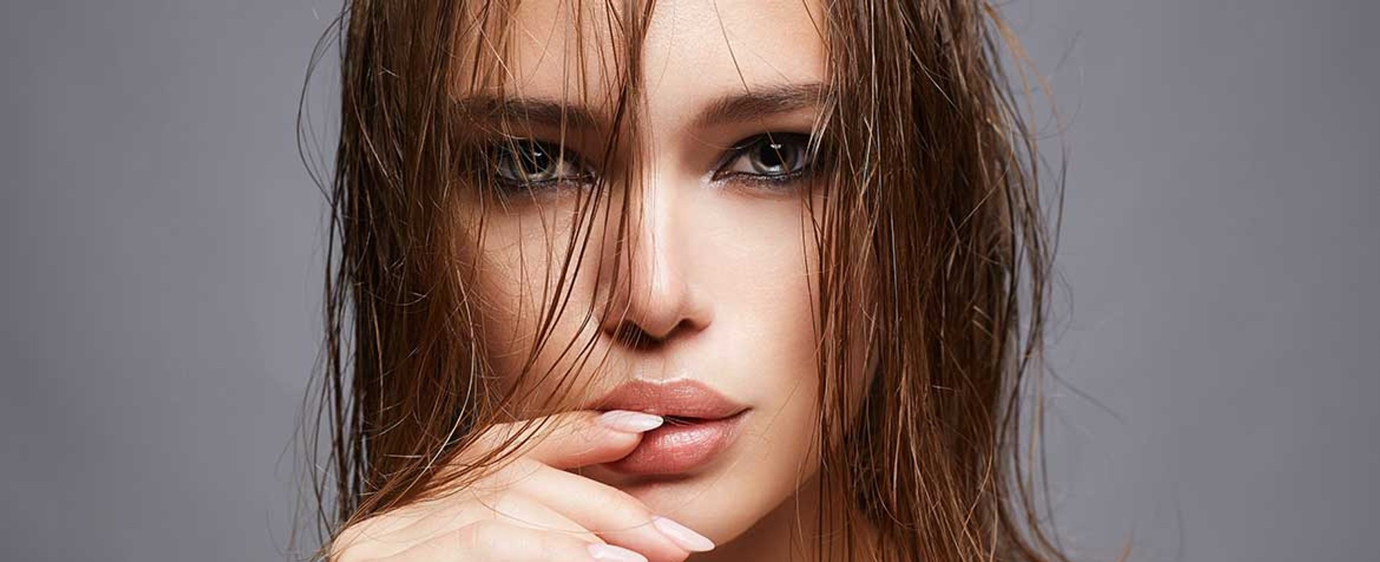 Modelo com cabelo molhado e olhar penetrante com dedo nos lbios