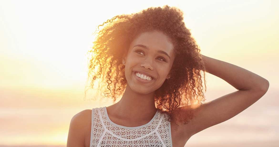 Modelo cacheada e morena enfrente ao som sorrindo