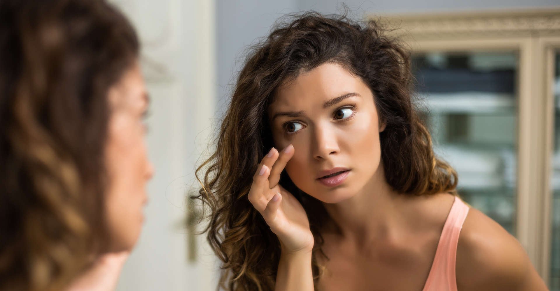 mulher examina olheiras em frente ao espelho