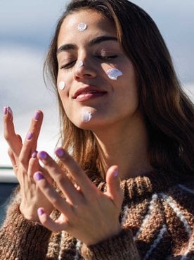 Modelo branca passando protetor solar no rosto