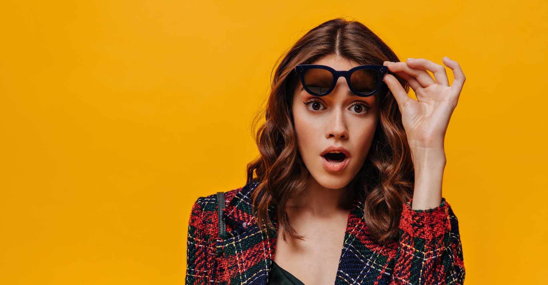 Modelo com cabelo ondulado e mechas loiras tirando o óculos de sol