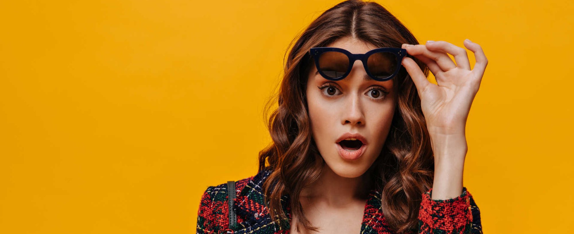 Modelo com cabelo ondulado e mechas loiras tirando o óculos de sol