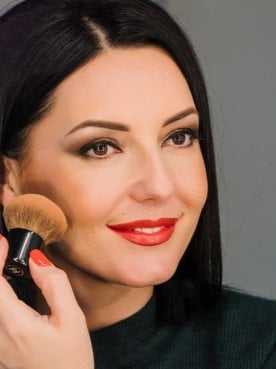 MOdelo branca com cabelo preto passando maquiagem no rosto