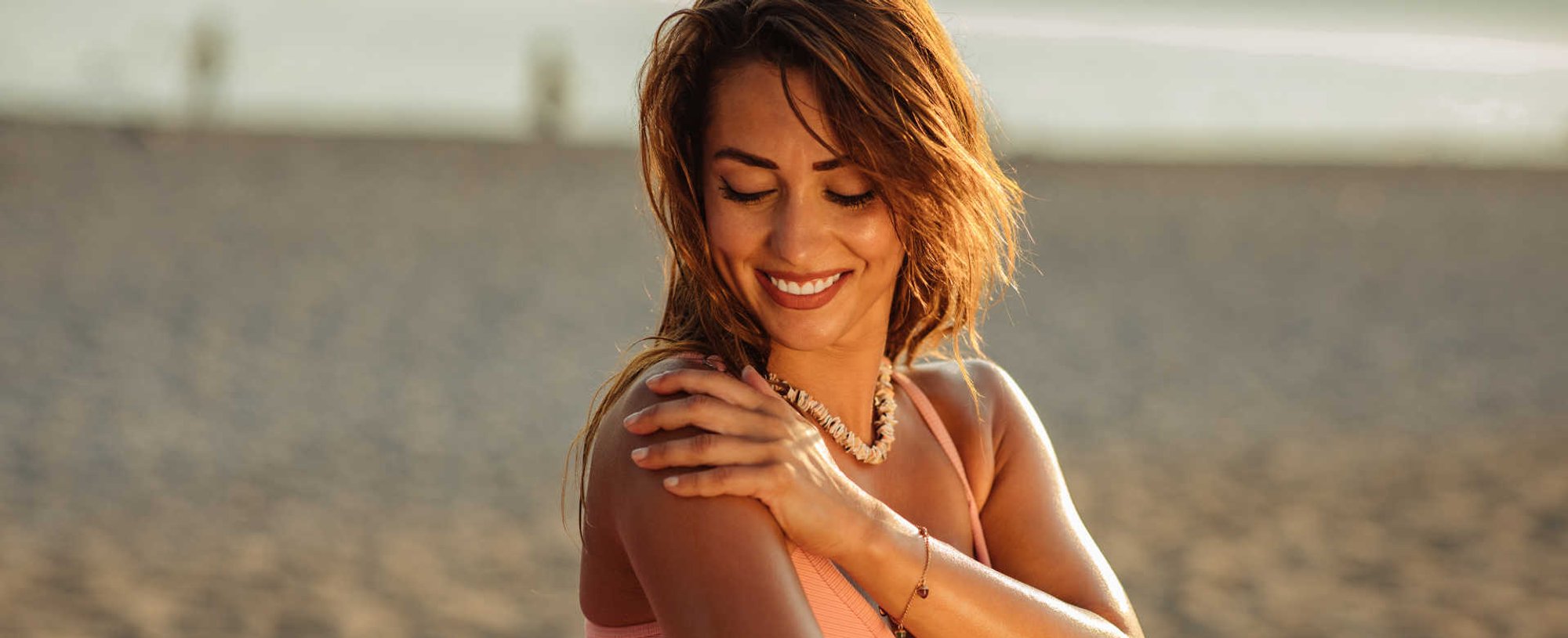 Modelo branca sorrindo passando protetor solar no braço