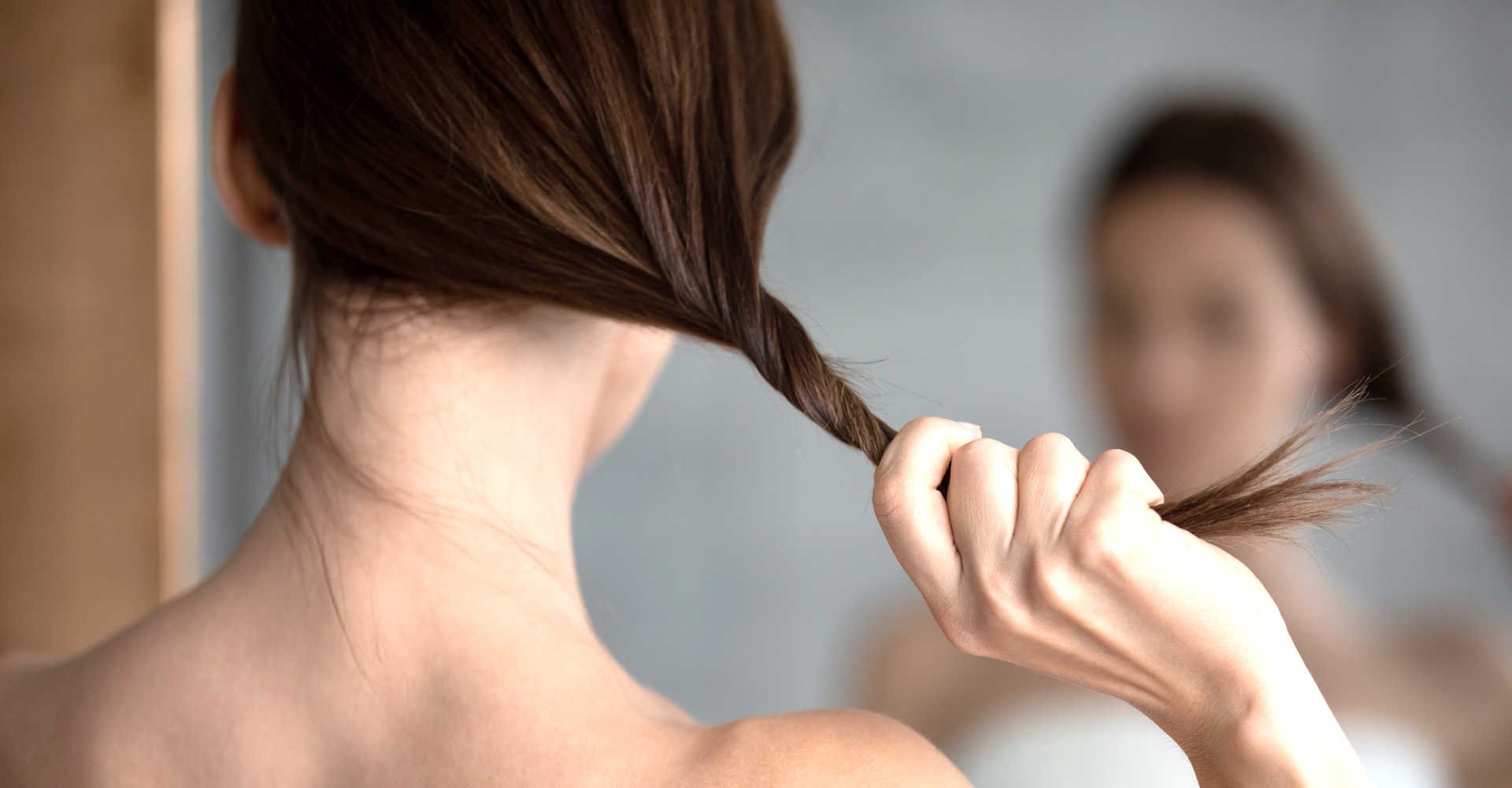 Modelo branca se olhando no espelho segurando seus cabelos