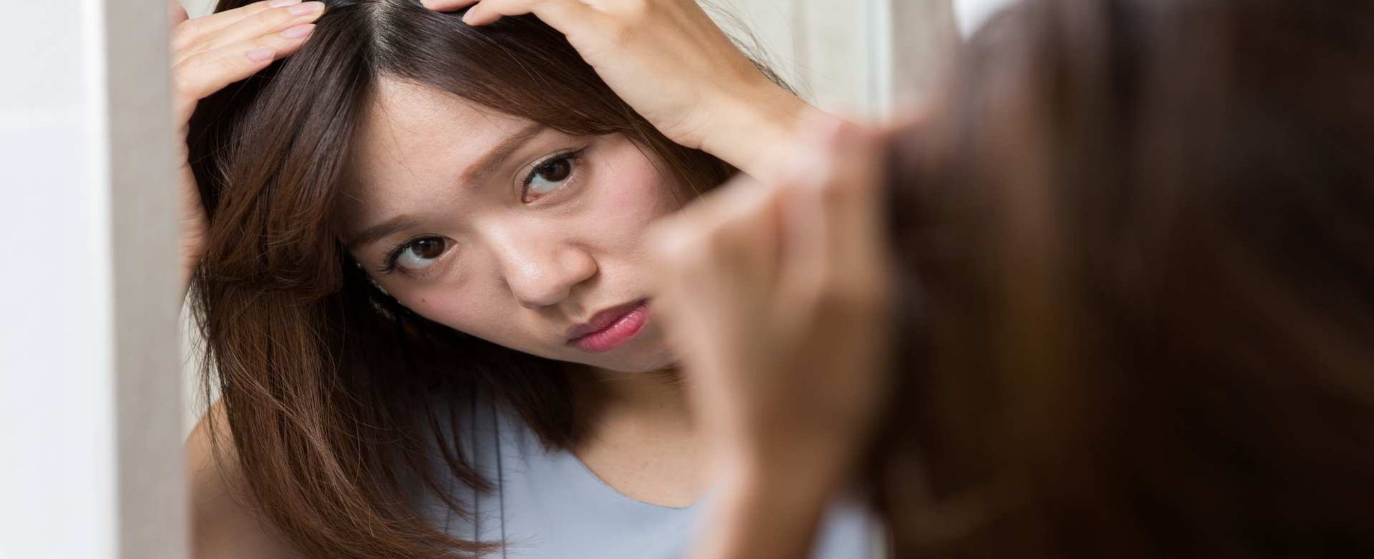 Modelo asiática olhando seu couro cabeludo pelo espelho