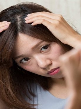 Modelo asiática olhando seu couro cabeludo pelo espelho
