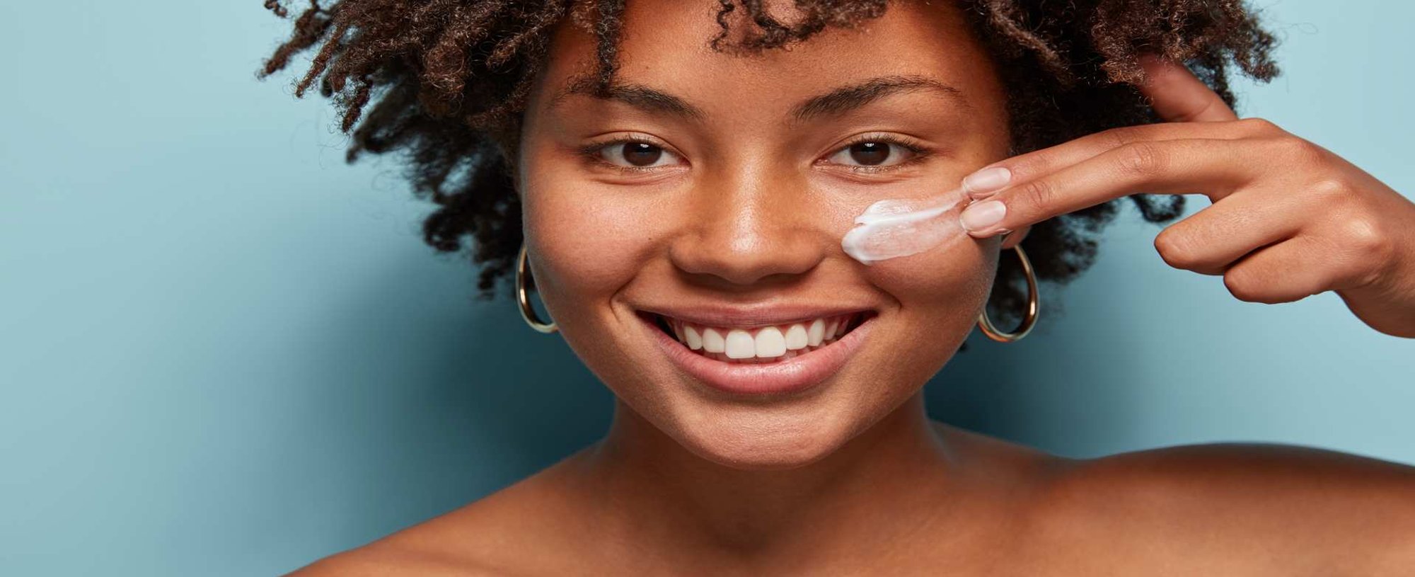 Modelo negra sorrindo passando creme no rosto