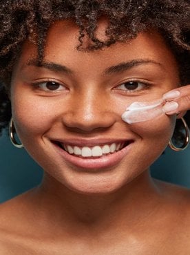 Modelo negra sorrindo passando creme no rosto