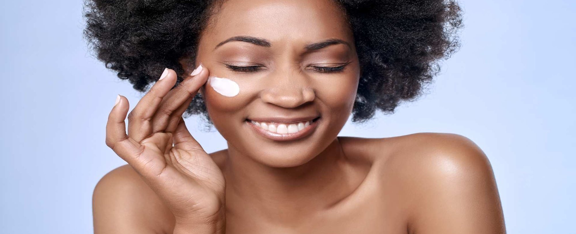 Modelo negra sorrindo passando creme no rosto