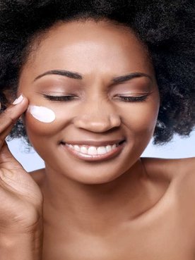 Modelo negra sorrindo passando creme no rosto