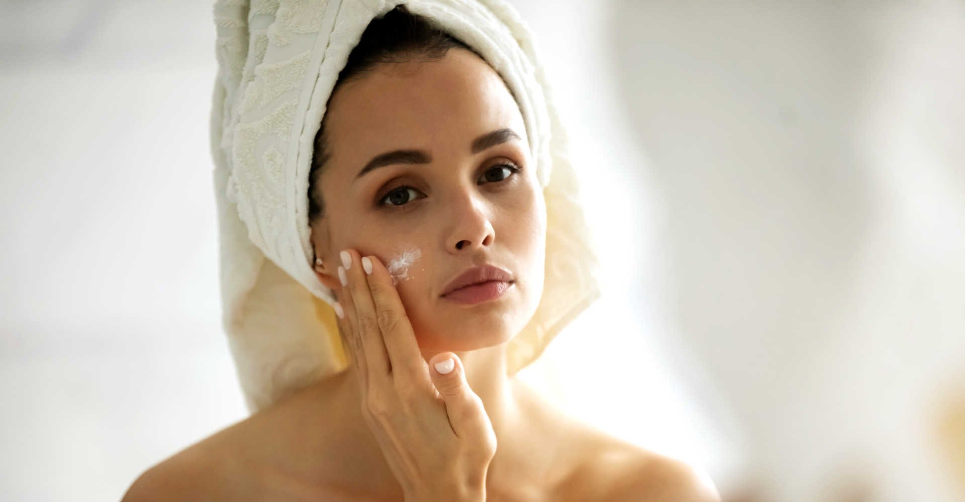 Modelo branca se olhando no espelho e passando creme