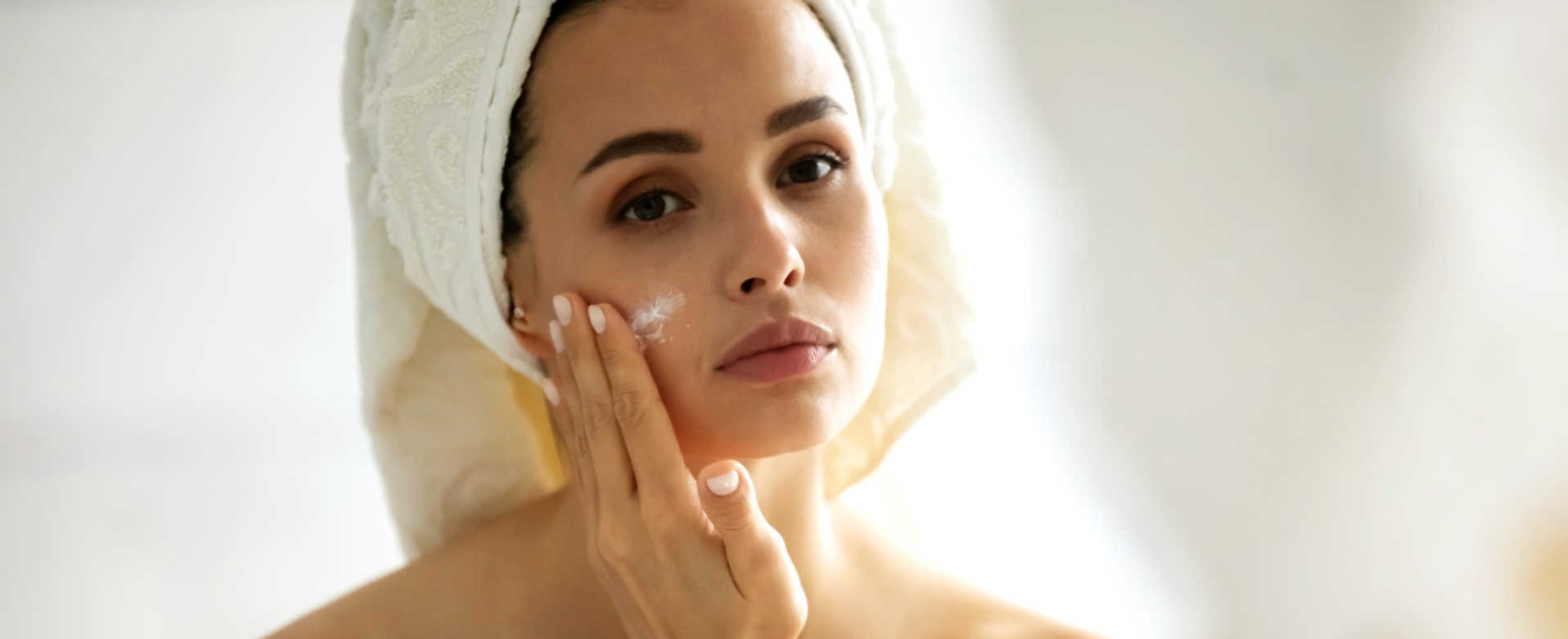Modelo branca se olhando no espelho e passando creme