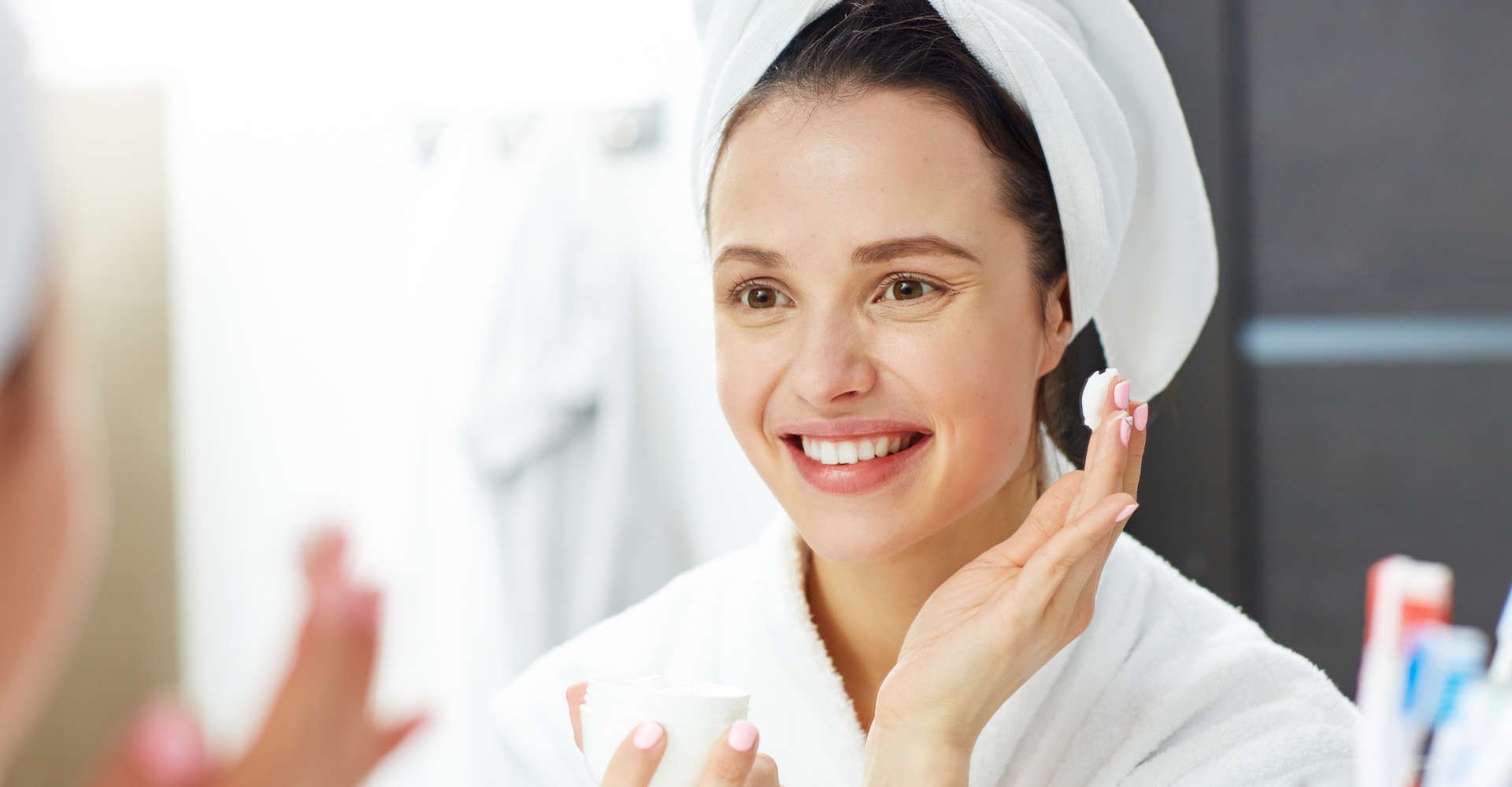 Modelo branca se olhando no espelho e passando creme